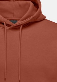 Rust-colored hoodie with a soft texture, featuring a drawstring hood and a ribbed neckline. The fabric appears to be cotton blend.