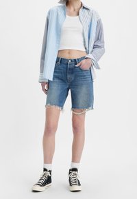 Chemise rayée bleu clair et gris sur un débardeur blanc, associée à un short en denim bleu déchiré et des baskets montantes noires.