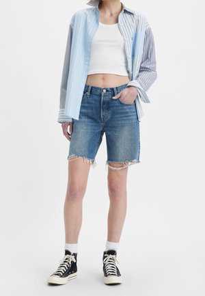 Chemise rayée bleu clair et gris sur un débardeur blanc, associée à un short en denim bleu déchiré et des baskets montantes noires.