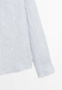 Sezione di camicia a maniche lunghe con sottili strisce verticali blu e bianche e polsino a righe abbinato su sfondo bianco.