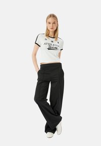 Camiseta corta blanca con detalles negros y estampado "equipo ATLÉTICO", combinada con pantalones de pierna ancha negros y zapatillas blancas.