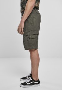 Pantaloni cargo verde oliva realizzati in tessuto leggero, dotati di due tasche laterali, dettagli con bottoni e un fit rilassato, abbinati a sneakers nere.