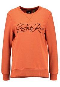 Sudadera naranja con cuello redondo, mangas largas y puños acanalados. Presenta un logotipo cursivo negro en la parte frontal. Textura de tela suave.