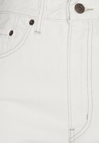 Tejido de denim blanco con textura visible y trama diagonal. Presenta un botón y costuras en tono cobre. Incluye un bolsillo frontal.