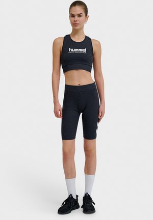 Donkergrijze sportset, bestaande uit een cropped tanktop met logo en hoge biker shorts, gecombineerd met zwarte sportschoenen en witte sokken.