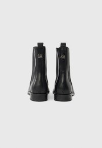 Černé kožené kotníkové boty s elastickými bočními panely, plochou podrážkou a malými poutky na natažení. Na bocích mají stříbrné logo.