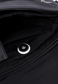 Černá kožená taška uvnitř s hladkým látkovým podšívkou, obsahující zipovou kapsu a kulatou bílou štítku Apple.