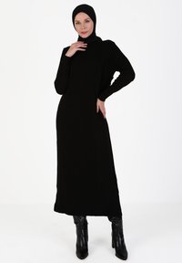 Black long-sleeve dress with ribbed texture, featuring a high neck and slim fit. Paired with knee-high black boots. Simple, elegant design.