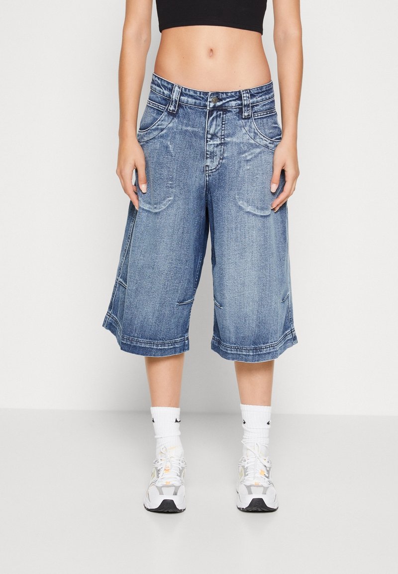 Denim culotter med en blekt blå tvätt, midjehöjd, sidofickor och uppvikta ben, kombinerade med vita sneakers och ankelsockor.