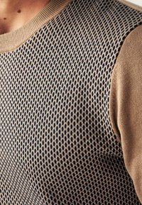 Gestrickter Pullover mit einem strukturierten Muster in Marineblau und Beige, mit einem gerippten Halsausschnitt und kontrastierender Farbe an den Schulternähten.