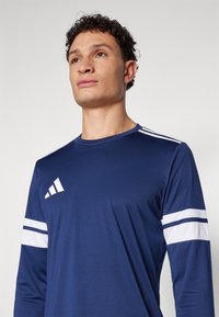 Marineblauw sportshirt met lange mouwen, gemaakt van lichtgewicht stof, met witte accentstrepen op de mouwen en een logo op de borst.