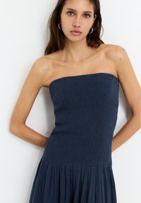 Trägerloses Marineblaues Kleid mit strukturiertem Oberteil und fließendem Rock. Das dehnbare Material weist gerüschte Details auf. Schlichtes Design mit lockerer Passform.