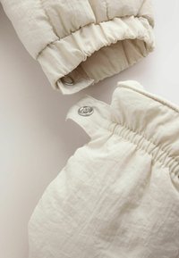 Close-up of cream-colored quilted jacket sleeves with elastic cuffs and metal snap button fasteners.