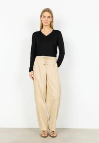 Čierny top s dlhým rukávom a výstrihom s vlnitým lemom, v kombinácii s béžovými širokými nohavicami s elastickým pásom a šnúrkou.