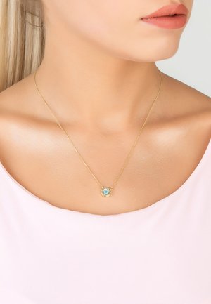 Gold necklace featuring a round pendant with a blue circular detail, worn against a light pink top, showcasing a fine chain design.