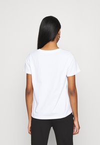 Camiseta de cuello redondo blanca hecha de algodón, con mangas cortas, un ajuste relajado y un dobladillo redondeado, vista desde la parte de atrás.