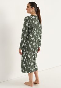 Lång grön nattklänning i mjukt tyg, med ett vitt mönster av skog och hjortar, med långa ärmar och rund halsringning.