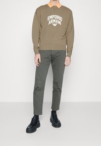 Pull vert olive avec le logo "Emporio Armani", col orange, associé à un pantalon vert olive et des chaussures noires épaisses. Texture lisse, coupe contemporaine.