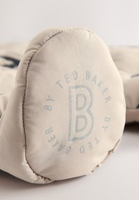 Beige vaahtokas taipeellinen tyyny, jossa on pyöreä muotoilu. Sisältää siniharmaan kohokuvioidun "Ted Baker" -brändin. Suora pinta ja ommellut reunat.