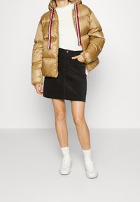 Puffjakke i metallisk guld, med hætte og kontrasterende rød, hvid og blå snore. Paret med en sort denimnederdel og hvide sneakers.