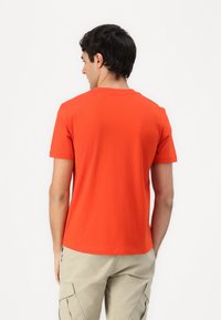 Camiseta de algodón roja con cuello redondo y mangas cortas, vista desde la parte de atrás. La tela parece suave y ligera.