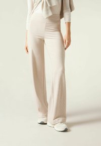 Pantalons larges en maille beige clair avec une taille haute, fabriqués dans un tissu texturé doux, associés à des baskets blanches.