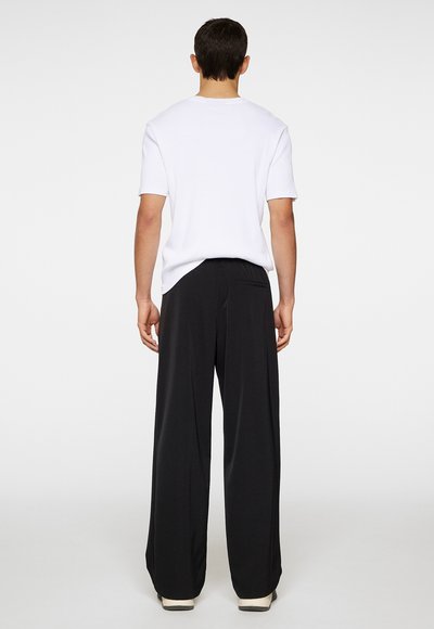 White short-sleeve t-shirt paired with black wide-leg pants. Pants feature a slight sheen, elastic waistband, and back pocket detail.