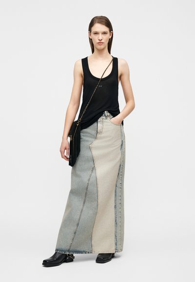 Γυναίκα που φοράει μαύρο αμάνικο τοπ, μακρύ δίχρωμο τζιν φούστα, μαύρες μπότες μέχρι τον αστράγαλο και μαύρη τσάντα χιαστί με λεπτομέρεια φούντας.