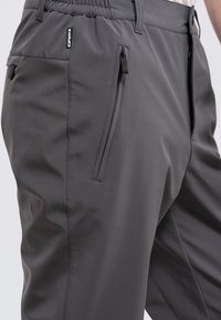 Graue Sporthosen aus glattem, dehnbarem Stoff. Mit Reißverschlusstaschen und eleganten schwarzen Zuglaschen sowie einem elastischen Bund.