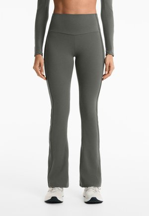 Leggings a vita alta svasati in tessuto grigio scuro con una trama liscia e dettagli delle cuciture laterali, abbinati a sneakers chiare.