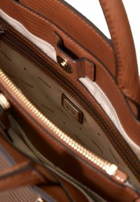 Sac à main marron en cuir texturé, ferrures dorées, doublure intérieure avec un logo "GUESS" répété, compartiment zippé visible.