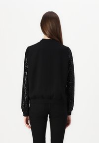 Schwarzer Sweatshirt mit Paillettenärmel, strukturierter Oberfläche, gerippten Bündchen und Saum, einfachem Kragen und taillierter Silhouette am Rücken.