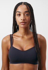 Svart bralette laget av et glattere, elastisk materiale. Har tynne, justerbare stropper og en V-formet halslinje, som gir en tettsittende passform.