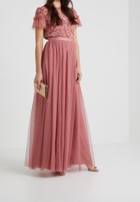 Roze tule maxi-jurk met pofmouwen, bloemom embroidery en een stippenpatroon. Gekoppeld aan een gouden clutch en nude sandalen met bandjes.