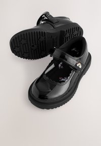 Glänzende schwarze Kinder-Mary-Jane-Schuhe mit sternenförmigen Sohlen, einem Einhorn-Print-Stoffeinsatz und einem Klettverschluss mit Regenbogen-Patch.