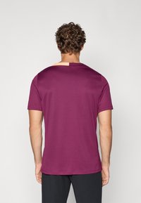 T-shirt de mangas curtas em tecido bordeaux profundo. Apresenta uma seção contrastante de cor clara na parte de trás do pescoço. Textura suave, ajuste casual.