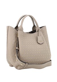 Sac en cuir beige avec des clous dorés, texture souple, partie supérieure arrondie, doubles poignées et détail de petite étiquette. Design robuste avec un fond plat.