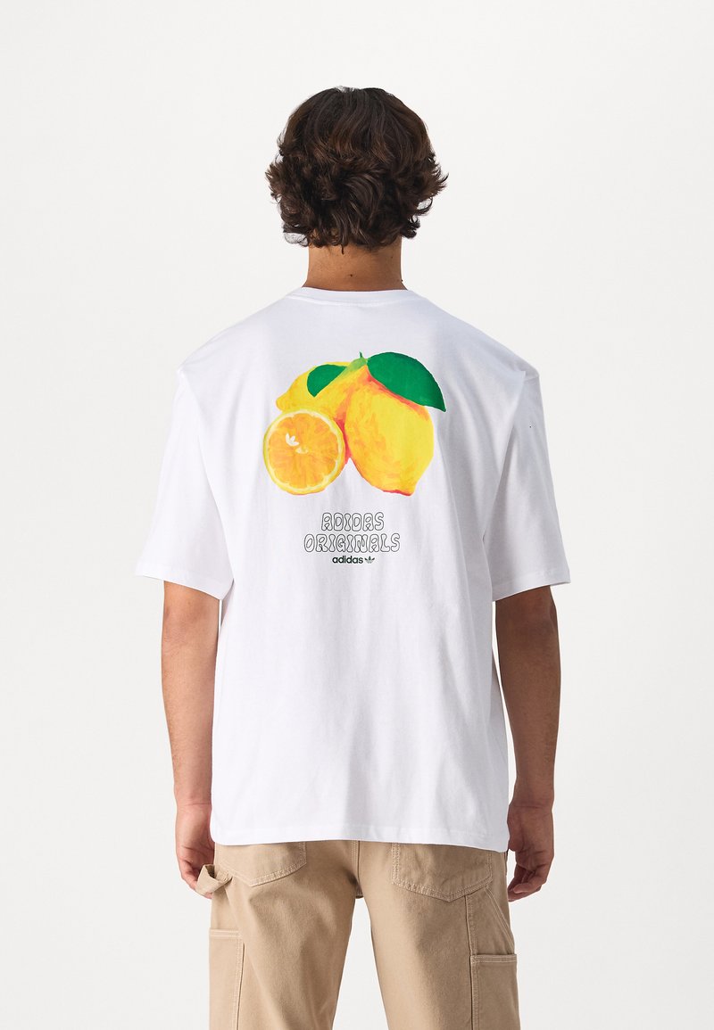 T-shirt bianca in cotone con una grafica colorata di limone e arancia sul retro, con la scritta "adidas Originals" stampata sottostante.