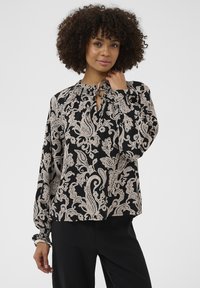 Svart blus med beige paisleymönster, långa ärmar, elastiska muddar och detalj med nyckelhål och halsband. Slät tyg och avslappnad passform.