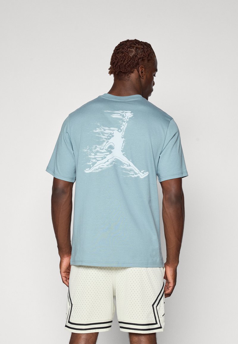 Gaiši zila kokvilnas T-kreklā ar baltu, stilizētu Jumpman logo uz muguras. Īsas piedurknes, apaļa kakla dizains un brīvs griezums.