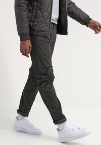 Mörkgrå vadderad jacka över en ljusgrå skjorta, kombinerad med mörka avsmalnande byxor och vita sneakers. Slät tyg med ribbade muddar.