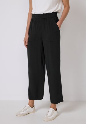 Zwarte wijde broek met een elastische tailleband en twee voorzakken, gemaakt van een zachte stof, gecombineerd met witte sportieve schoenen.