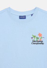 Svijetloplavi pamučni majica s okruglim izrezom, kratkim rukavima i šarenim cvjetnim logom s natpisom "Palm Springs Championship."