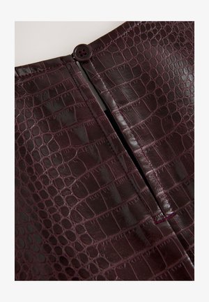 Krilo iz umetnega usnja barve bordo z teksturo krokodila, ki ima sredinski zadrgo in okrogel gumb na vrhu.