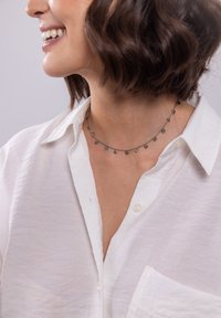 Silberne Halskette mit kleinen runden Anhängern, getragen über einem weißen Hemd mit Knöpfen, das eine feine Kette und dezente Details zeigt.