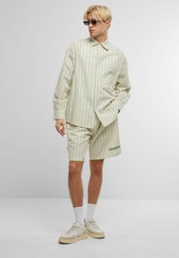 Rutet lys grønn skjorte med knappelukking og lommepatch, kombinert med matchende shorts. Brukt med joggesko og solbriller.