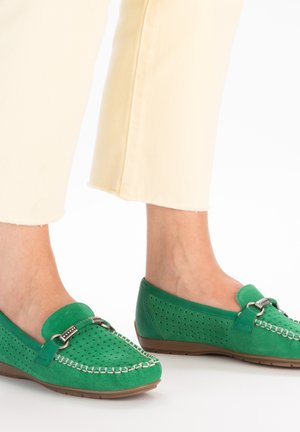 Grønne fløjl loafers med perforeret design, accentueret af en metal spænde og en kontrasterende lysebrun gummisål. Stylized med cremede bukser.