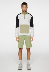 Let åndbar pullover med høj krave, hvide og marineblå ærmer samt en olivengrøn lomme foran. Sammen med matchende olivenfarvede shorts.