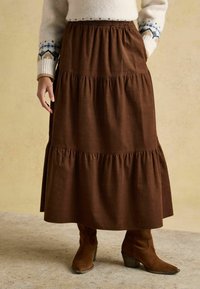 Brun, flerstegs maxikjol med elastisk midjeresår, tillverkad av ett mjukt, texturerat tyg. Matchas med bruna klackade ankelboots.