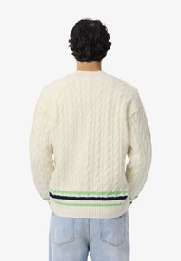 Maglione crema a maglia cable con superficie texturizzata, caratterizzato da strisce orizzontali in verde e blu navy lungo l'orlo inferiore.